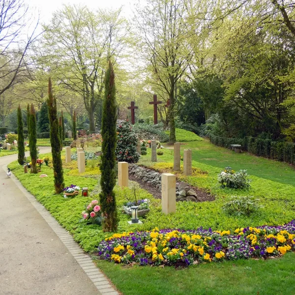 Blick auf gepflegte Gräberfelder mit Blumen, Bäumen und Grabsteinen auf dem Friedhof.