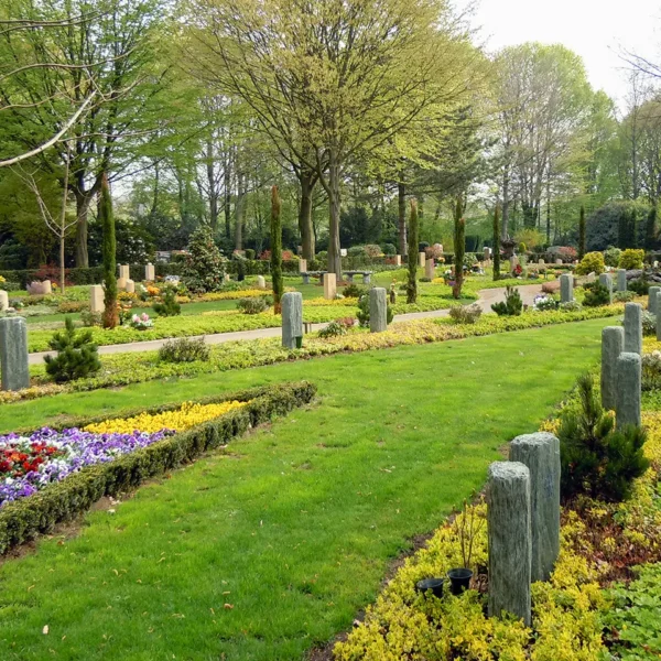 Blick auf gepflegte Gräberfelder mit Blumen, Bäumen und Grabsteinen auf dem Friedhof.