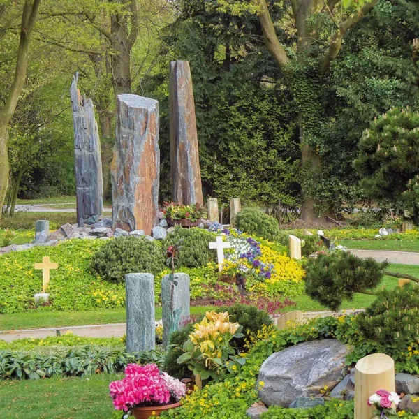 Blick auf gepflegte Gräberfelder mit Blumen, Bäumen und Grabsteinen auf dem Friedhof.