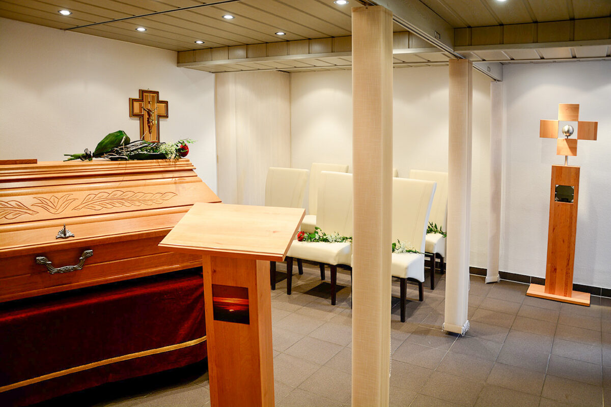 Aufbahrungsraum mit Sarg, Rednerpult und Sitzplätzen.